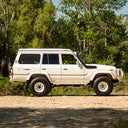 White SUV parked on a dirt road with trees in the background