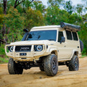 Beige Toyota SUV with roof rack on a dirt road surrounded by trees