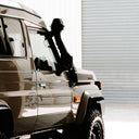 Silver SUV parked in front of a white building with a person wearing a hat and sunglasses inside.