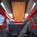 Back of a red vehicle with an open roof, showing wooden paneling and a clear sky.