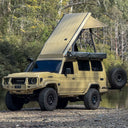 Beige Toyota SUV with a rooftop tent parked near a body of water with trees in the background