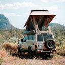 Beige 78 vehicle trooper with a rooftop tent in a natural landscape with mountains.