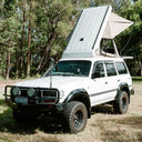 White SUV with a rooftop tent in a forest setting