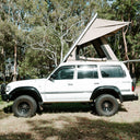 White SUV with a rooftop tent parked in a wooded area