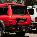Red Land Cruiser vehicle with a white van in the background