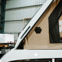 Beige roof tent on a white vehicle with visible branding against a blurred industrial background