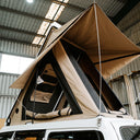 Beige rooftop tent attached to a vehicle inside a warehouse.