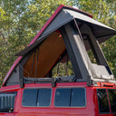 Red vehicle with an open roof top tent against a forest background