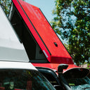 Red car roof tent attached to a white car with trees in the background